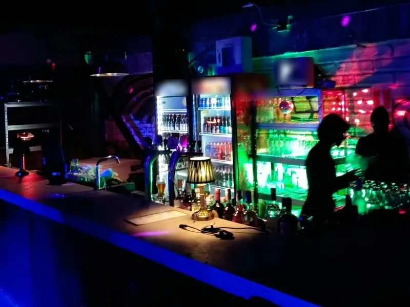 Bar con barra iluminada, neveras y licores, en ambiente nocturno
